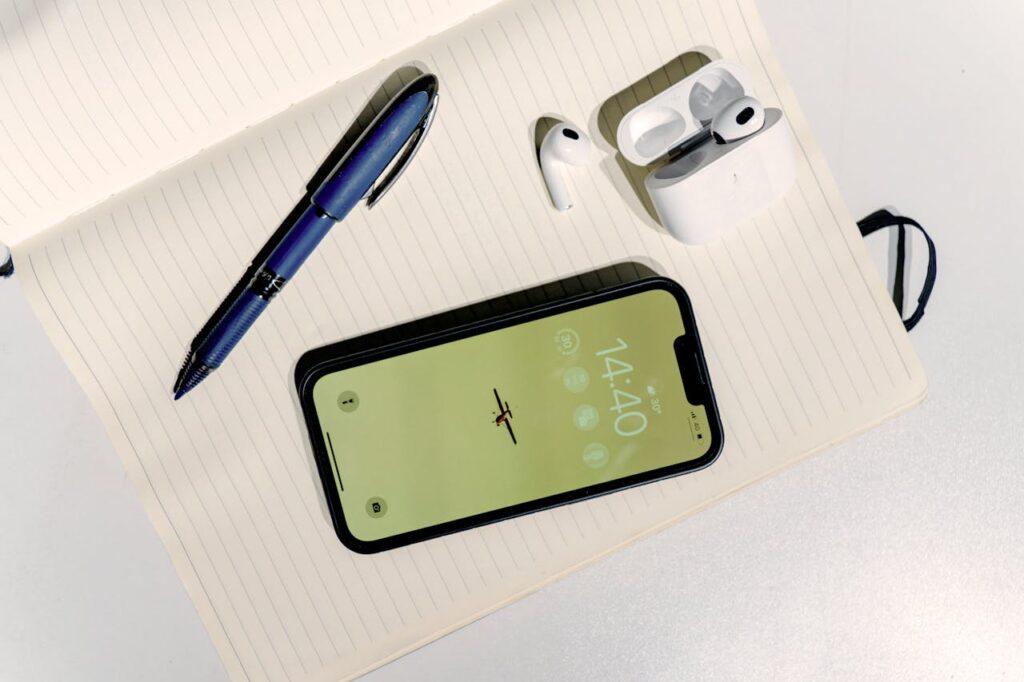 An iphone, pen and earphones are on a notebook